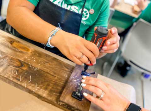 banner-image-mobile Guests assembling a wood sign using a power tool